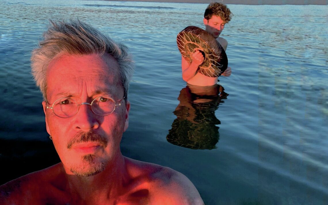 Dennis J. Coenraad en daarachter een andere man. Ze staan beide in het water.
