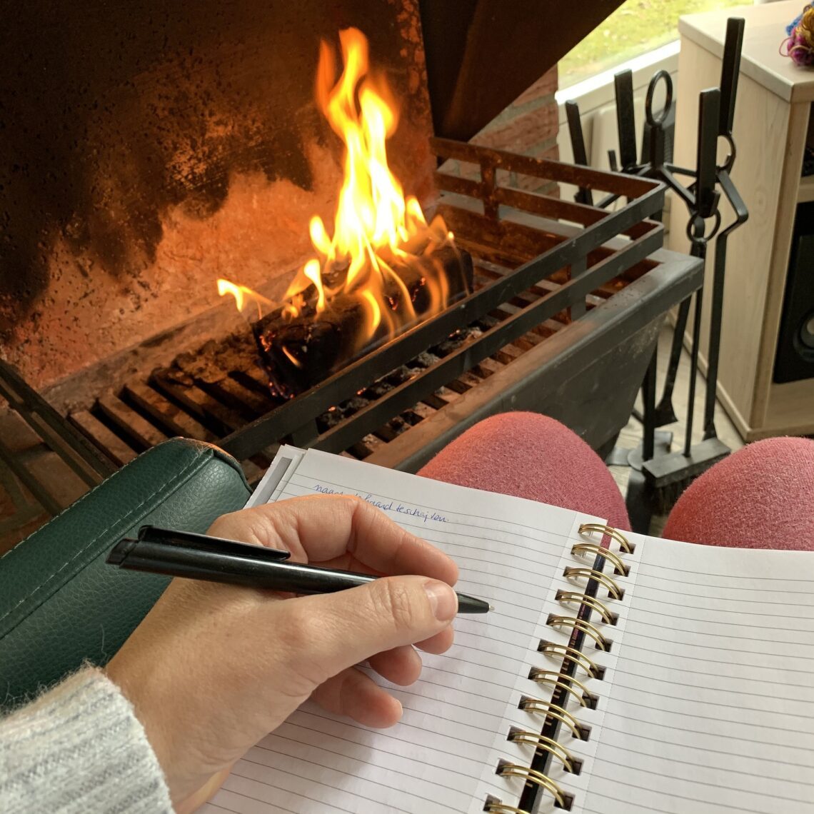 Persoon die aan het schrijven is in een notitieboekje voor een houtkachel.